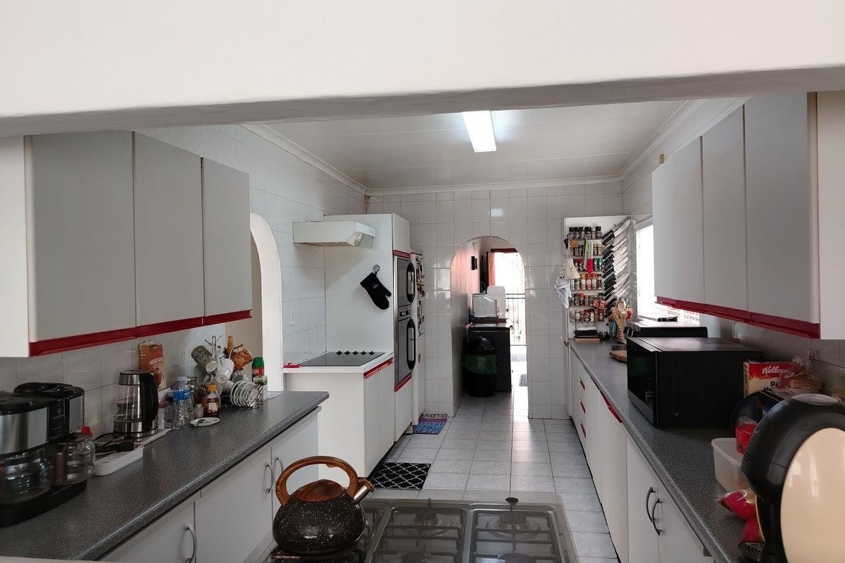 A functional galley-style kitchen featuring white cabinetry with red accents, tiled walls, and built-in cooking appliances, offering a practical layout for meal preparation.