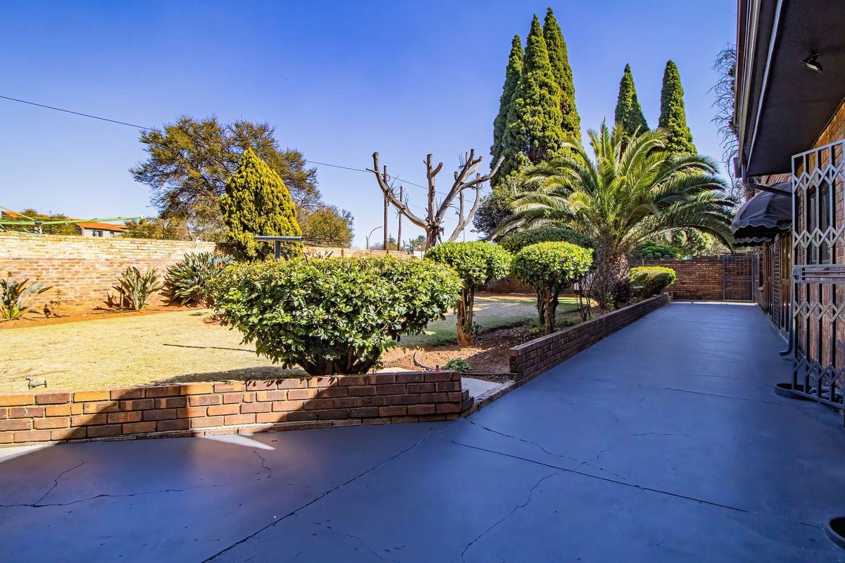 A spacious rear garden featuring a paved patio area, established landscaping, and a brick boundary wall, providing a private outdoor space.