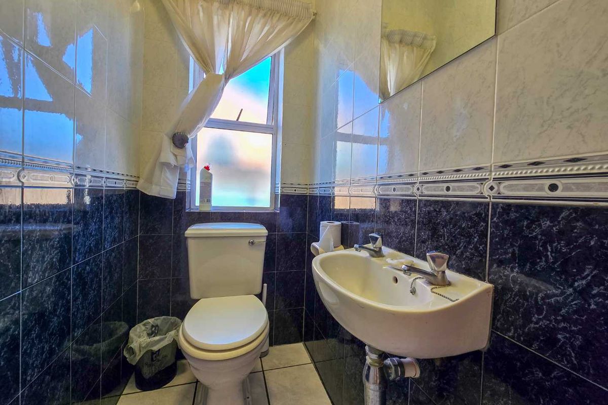 A compact bathroom featuring a wall-mounted basin, a standard toilet, and floor-to-ceiling tiled walls with a decorative border.