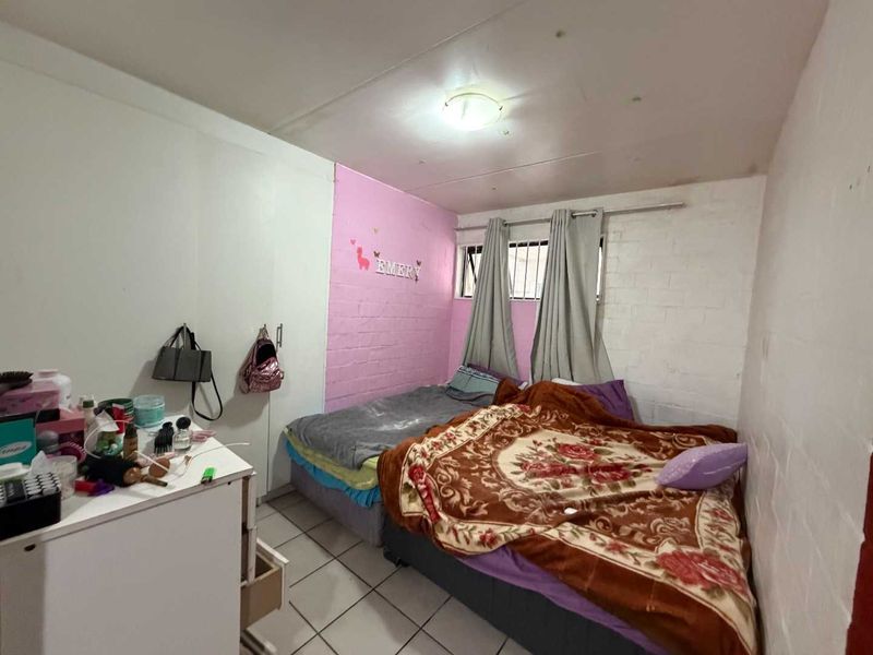 A bedroom featuring tiled flooring, a built-in wardrobe, and security bars on the window. The room requires cosmetic updates to improve its overall condition.