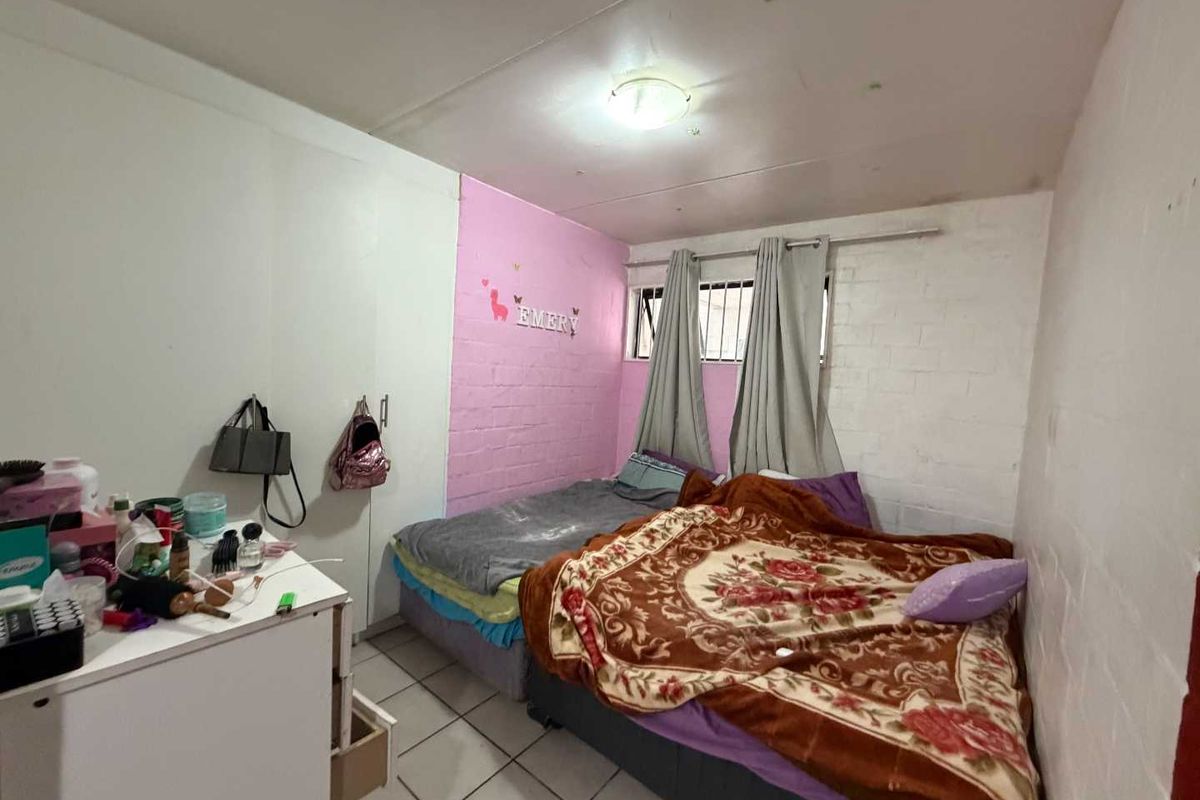 A bedroom featuring tiled flooring, a built-in wardrobe, and security bars on the window. The room requires cosmetic updates to improve its overall condition.