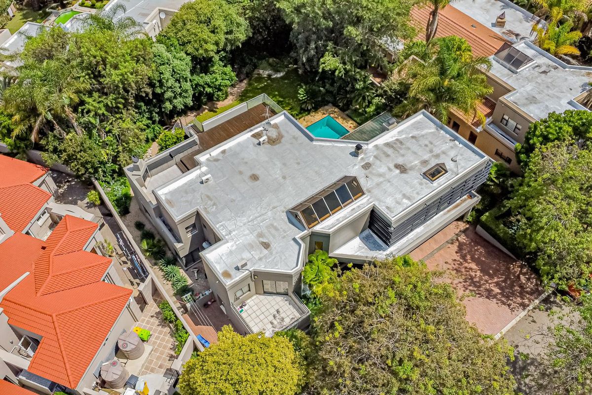 Aerial view of the property showcasing the flat roof structure, skylights, swimming pool, and surrounding landscaped garden area.