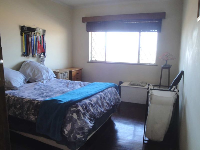 A standard bedroom featuring dark wood flooring and a window with security bars and a wooden pelmet.