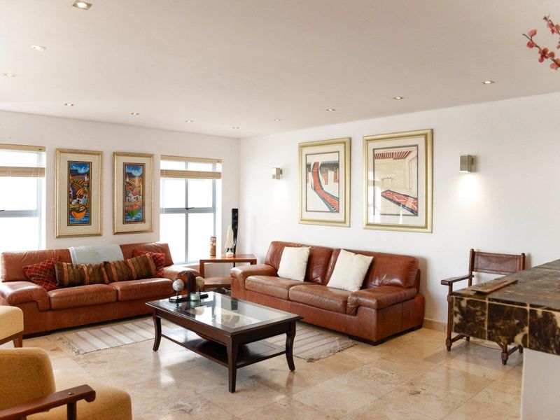 A spacious living room featuring polished stone tile flooring, recessed downlighting, and large windows that provide ample natural light.