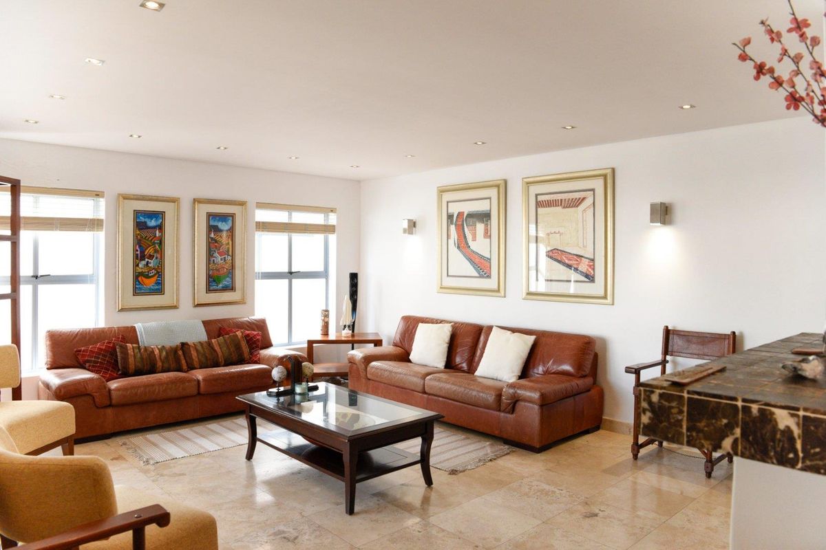 A spacious living room featuring polished stone tile flooring, recessed downlighting, and large windows that provide ample natural light.