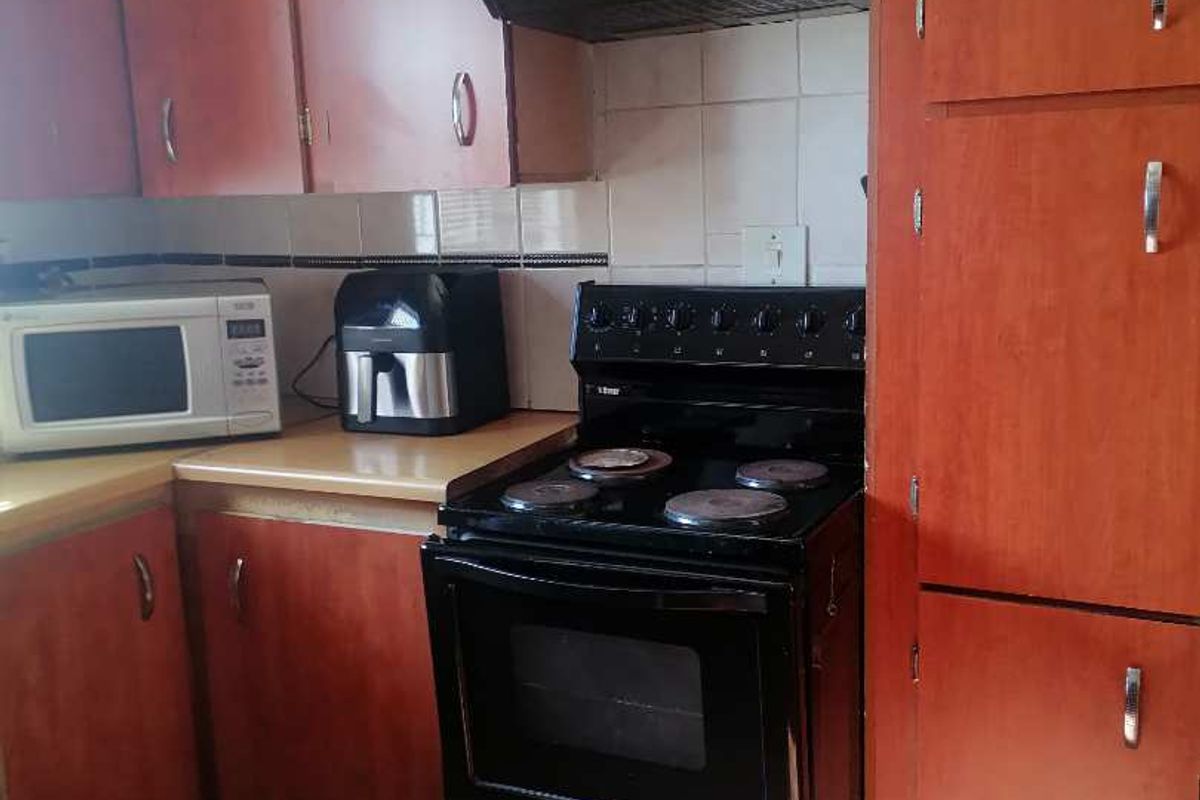 A functional kitchen featuring wood-finish cabinetry, a built-in extractor fan, and tiled flooring, offering a practical layout for daily meal preparation.