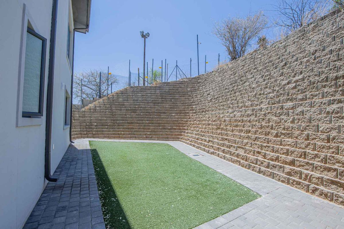 A private rear garden area featuring a tiered concrete block retaining wall, paved walkway, and low-maintenance artificial turf lawn.