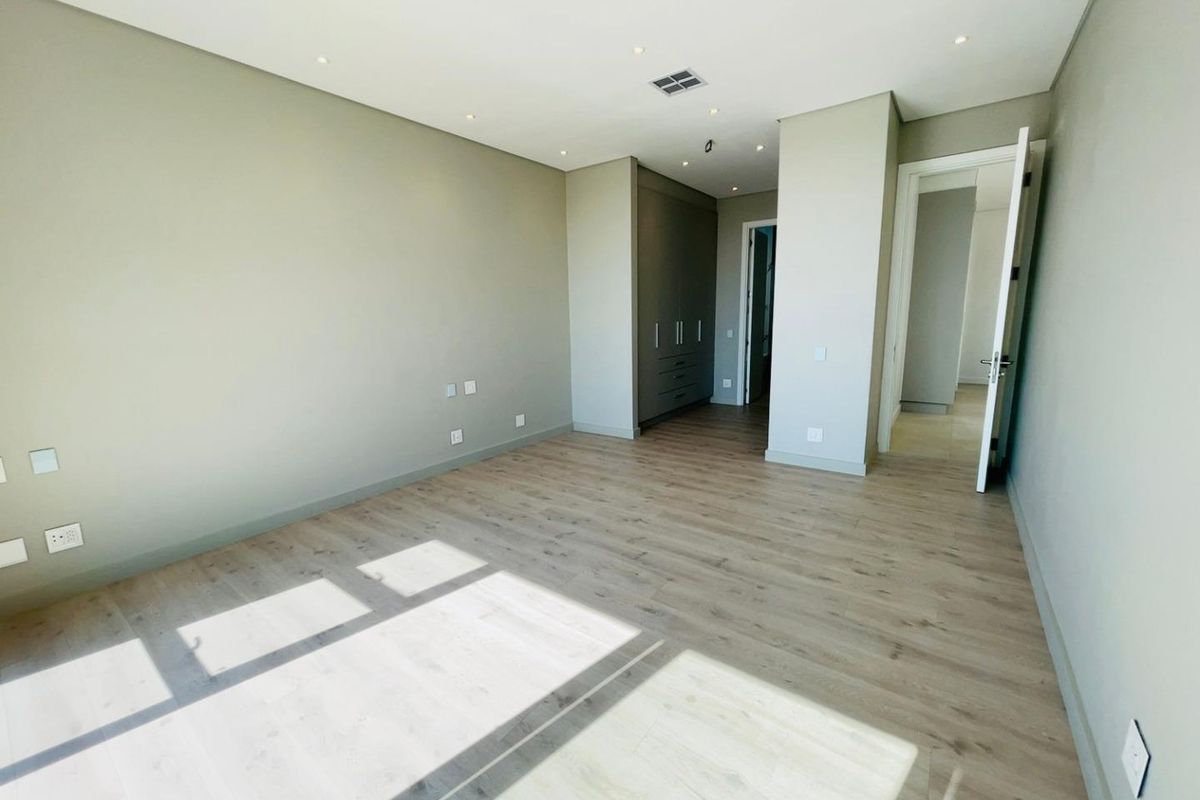 A bright, modern bedroom featuring neutral walls, light wood-look flooring, recessed ceiling lighting, and built-in cabinetry.