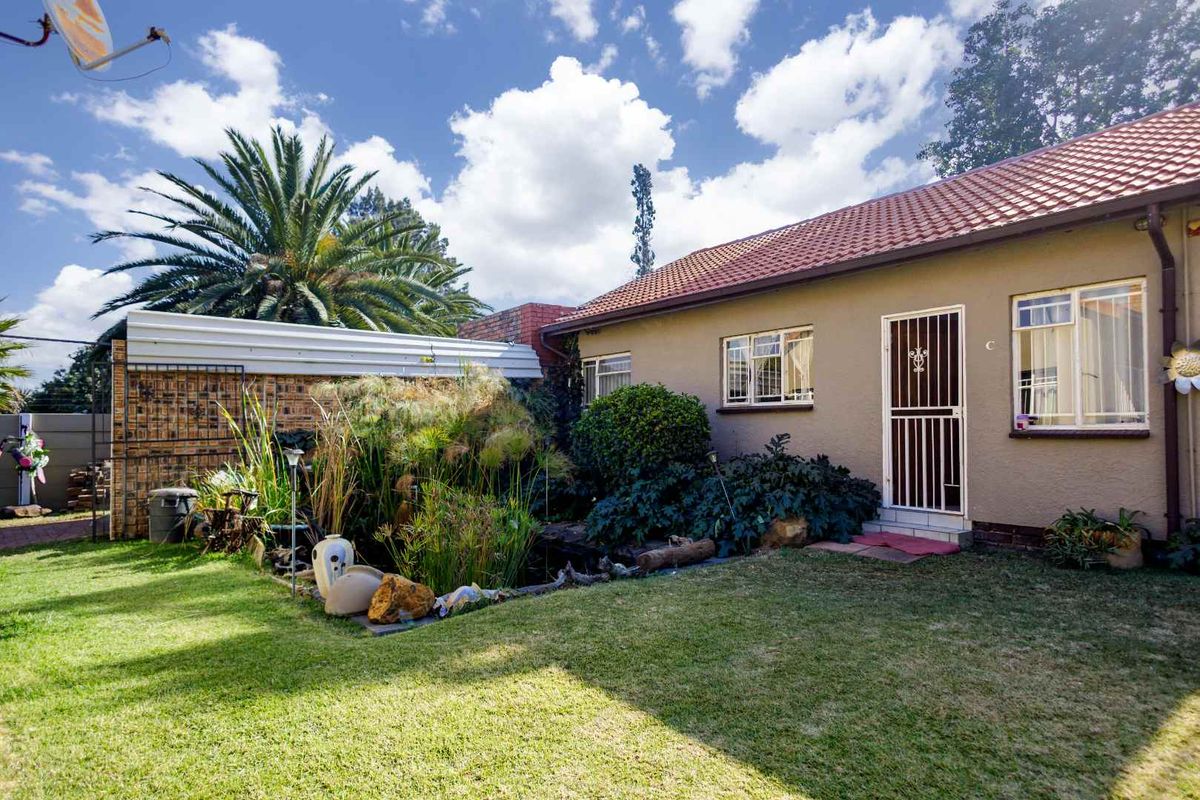 Rear view of the property featuring a landscaped garden, a small pond, and a tiled roof structure with security gates and window bars.