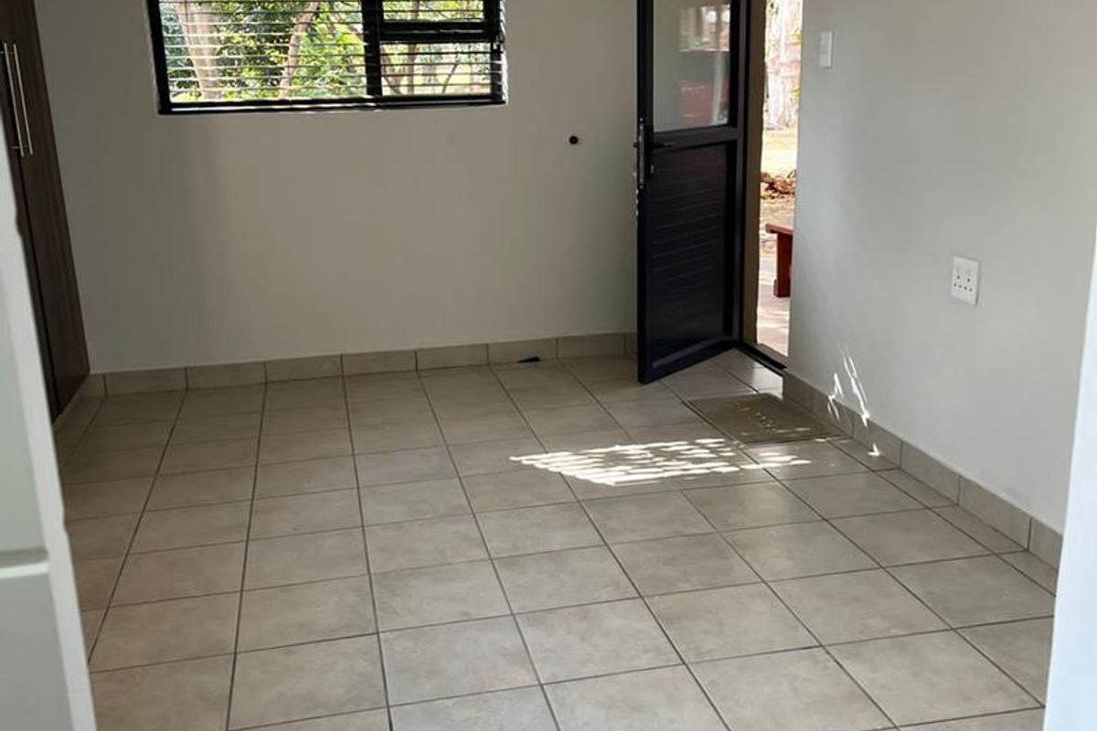 A bright, empty bedroom featuring neutral tiled flooring, a built-in cupboard, and direct access to the exterior through a glass-panelled door.