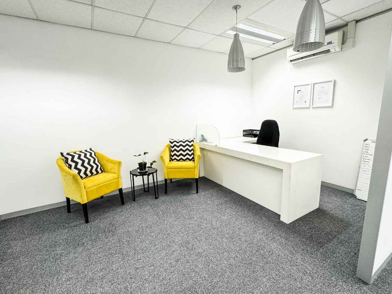 A professional office space featuring a built-in reception desk, carpeted flooring, suspended ceiling with integrated lighting, and a wall-mounted air conditioning unit.