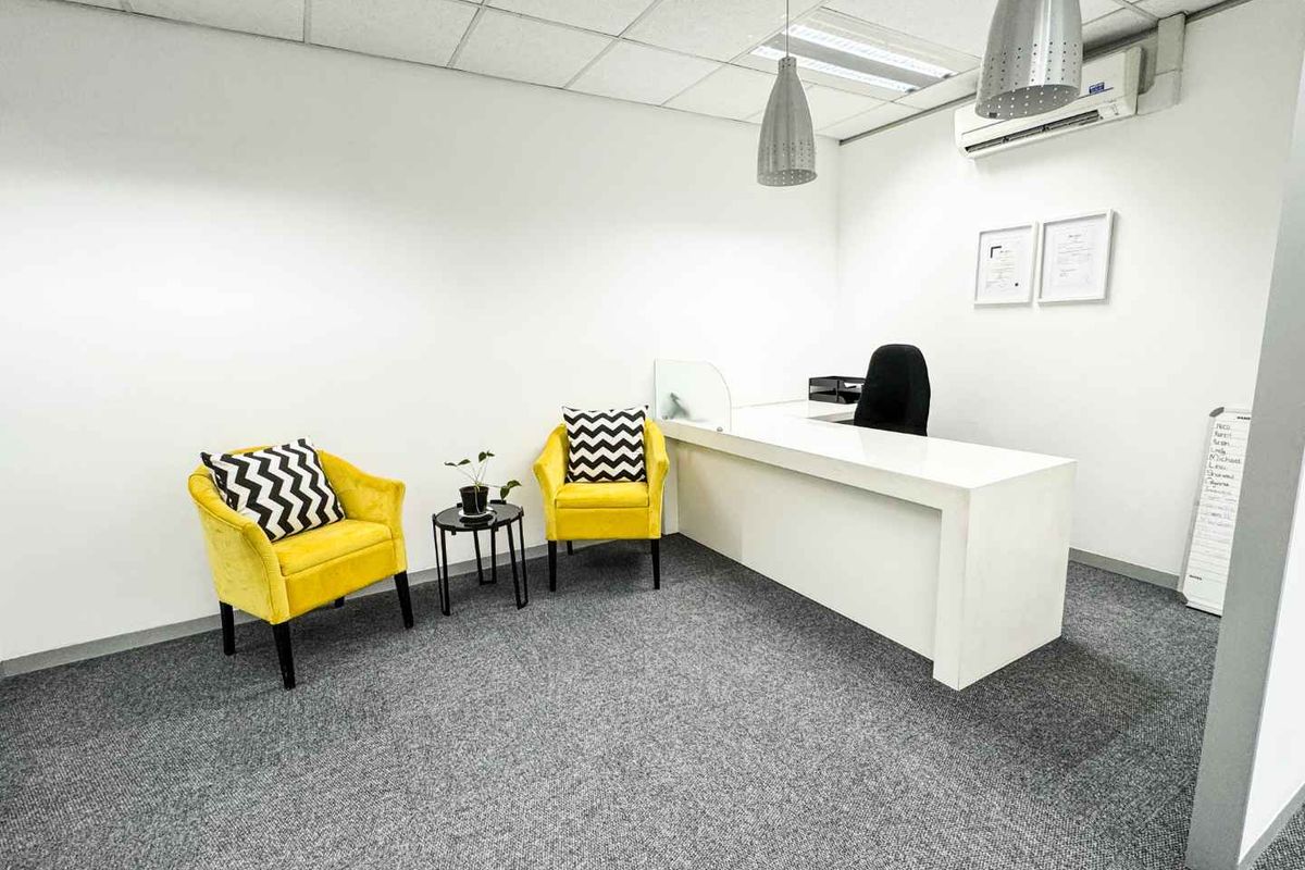 A professional office space featuring a built-in reception desk, carpeted flooring, suspended ceiling with integrated lighting, and a wall-mounted air conditioning unit.