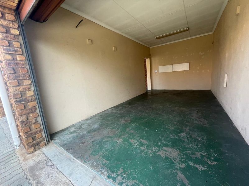 An empty, single-car garage featuring a painted concrete floor and basic lighting, showing signs of wear on the walls and floor.