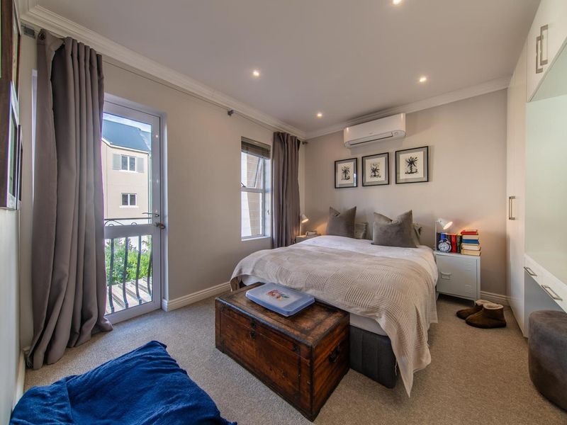 A well-maintained bedroom featuring built-in cupboards, recessed lighting, a split-system air conditioner, and direct access to a private balcony through a glass door.
