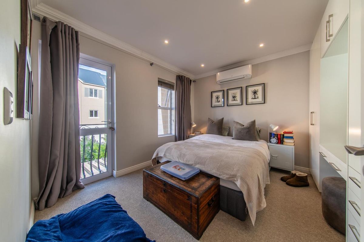 A well-maintained bedroom featuring built-in cupboards, recessed lighting, a split-system air conditioner, and direct access to a private balcony through a glass door.
