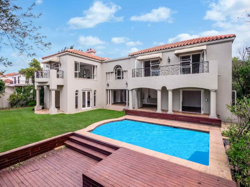 Rear view of a two-story residence featuring a swimming pool, timber decking, balconies with wrought iron railings, and a landscaped garden.