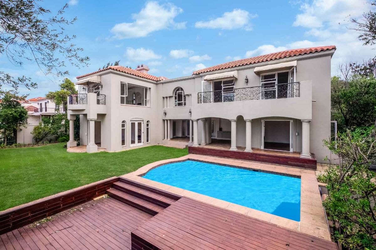 Rear view of a two-story residence featuring a swimming pool, timber decking, balconies with wrought iron railings, and a landscaped garden.