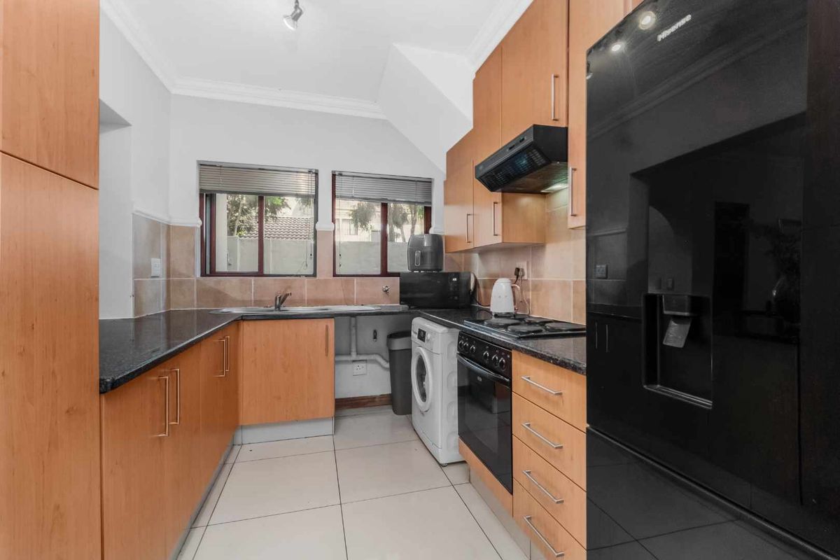 A functional kitchen featuring wood-veneer cabinetry, dark granite countertops, a built-in oven with extractor fan, and tiled flooring.