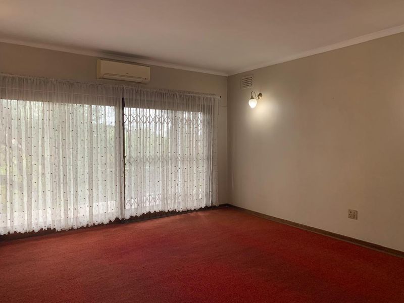 An empty living room featuring red carpet flooring, a wall-mounted air conditioning unit, and a large sliding glass door with a security gate.