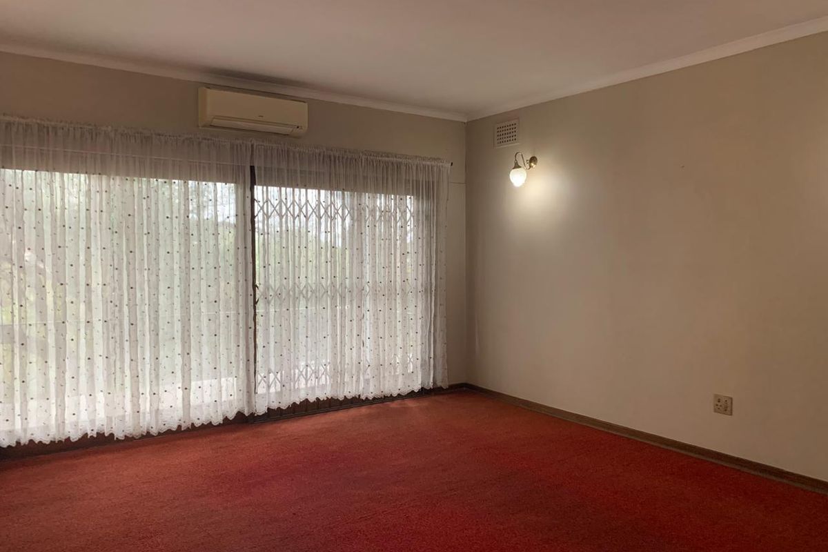 An empty living room featuring red carpet flooring, a wall-mounted air conditioning unit, and a large sliding glass door with a security gate.