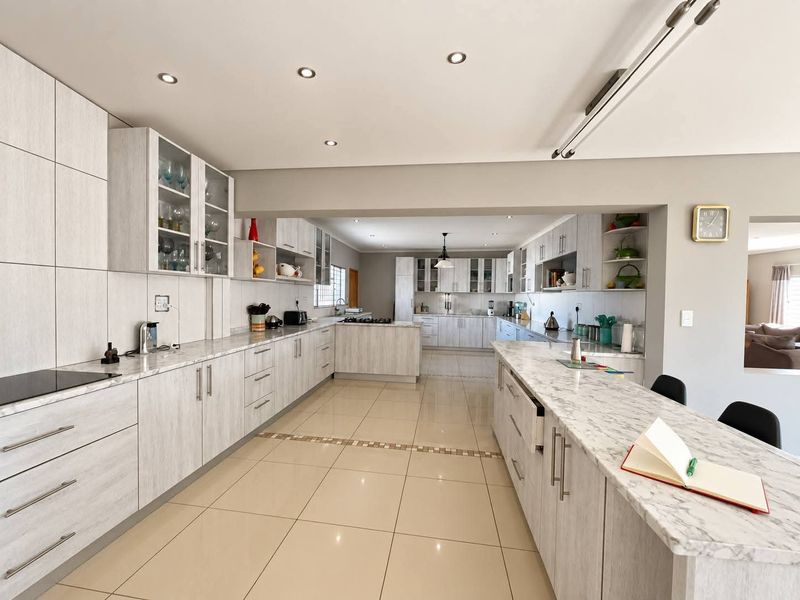Spacious, modern kitchen featuring extensive built-in cabinetry, stone countertops, a large central island, and neutral tiled flooring with recessed lighting throughout.