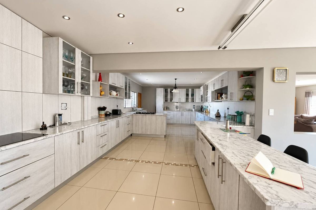 Spacious, modern kitchen featuring extensive built-in cabinetry, stone countertops, a large central island, and neutral tiled flooring with recessed lighting throughout.