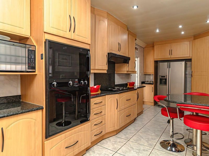 A well-appointed kitchen featuring light wood cabinetry, granite countertops, integrated appliances including an oven and microwave, and tiled flooring.