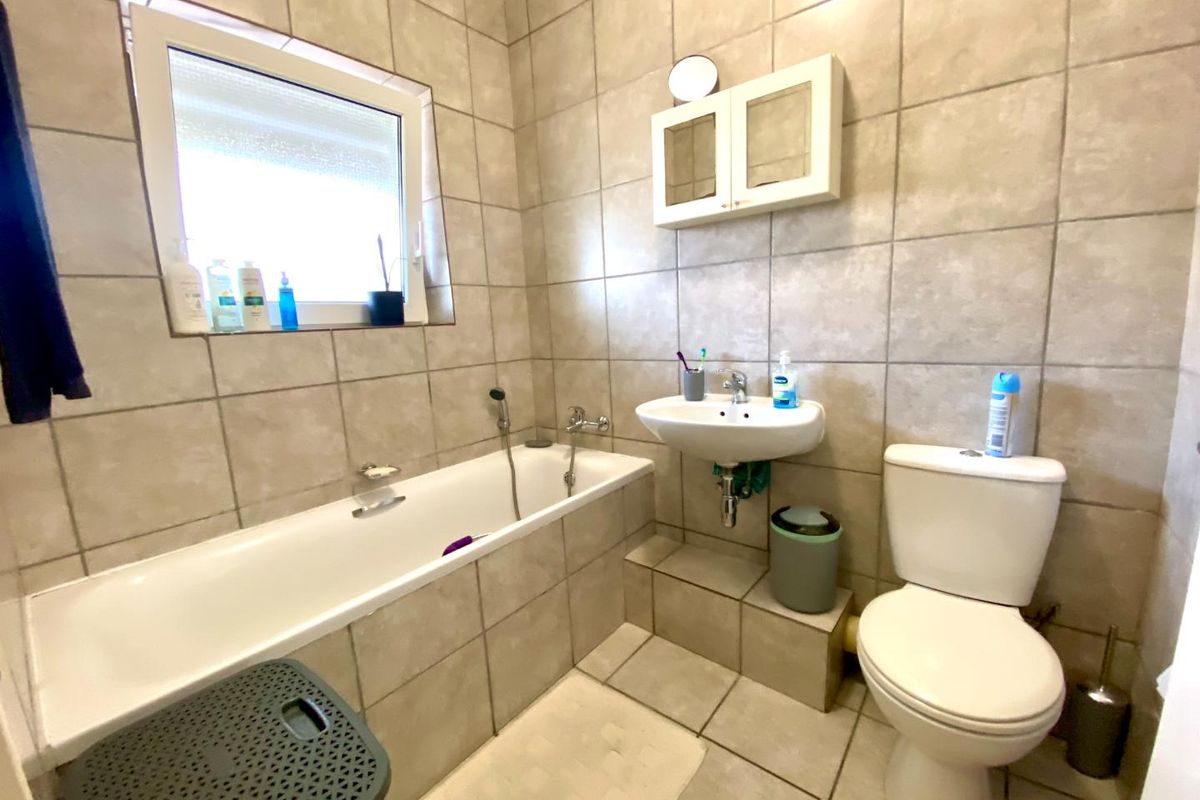 A functional bathroom featuring tiled walls and flooring, a standard bathtub, a wall-mounted basin, and a toilet.