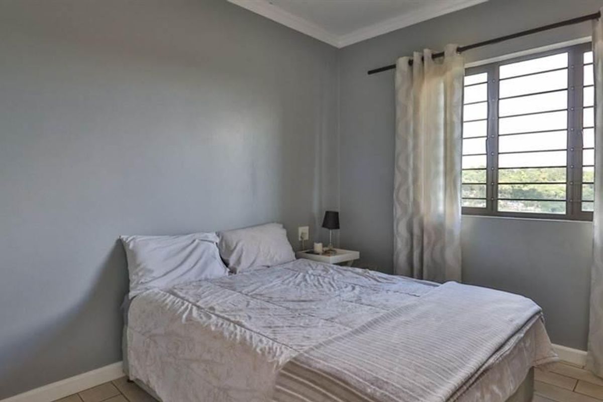 A bedroom featuring tiled flooring, neutral grey walls, and a window fitted with security bars.