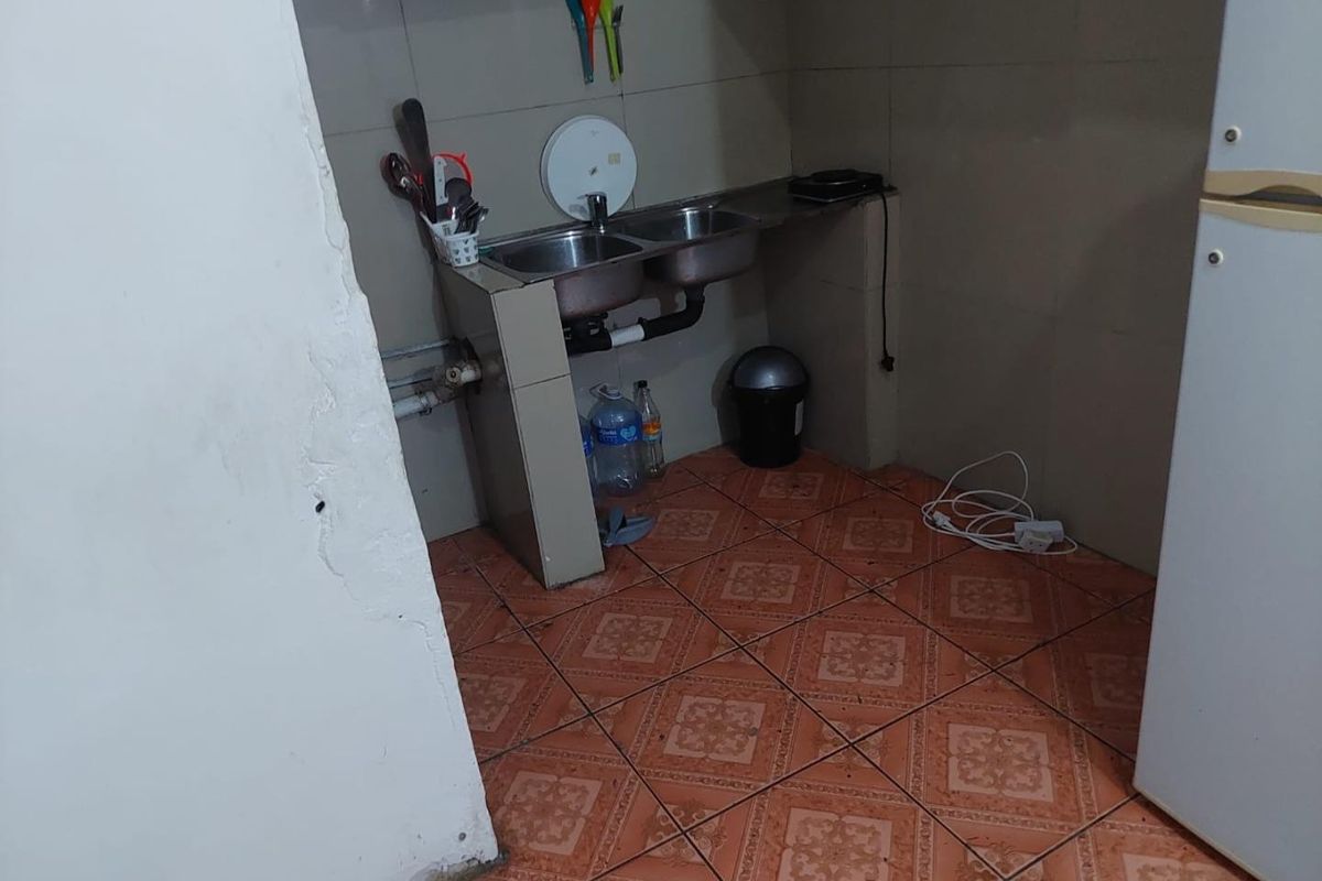A basic kitchen area featuring a double stainless steel sink, tiled splashback, and tiled flooring, requiring maintenance and cosmetic updates.