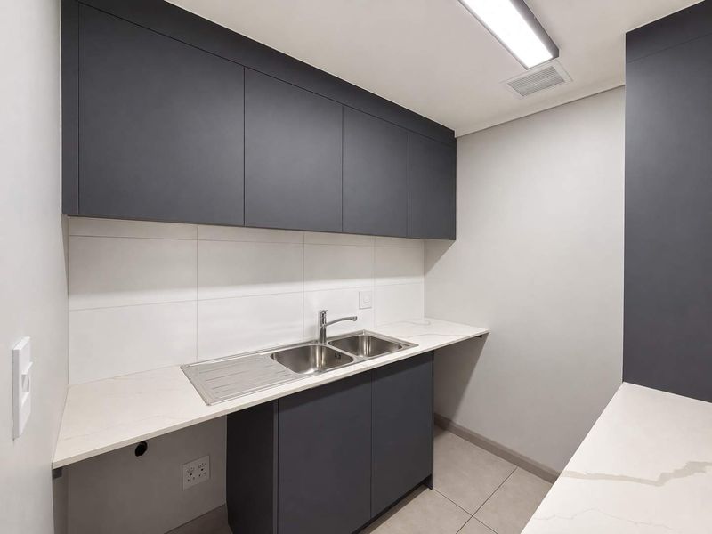 Modern scullery featuring sleek dark cabinetry, stone countertops, a stainless steel double sink, and clean tiled finishes.