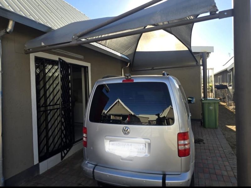 Rear exterior area featuring a paved driveway, shade sail covering, and a secure entrance gate.