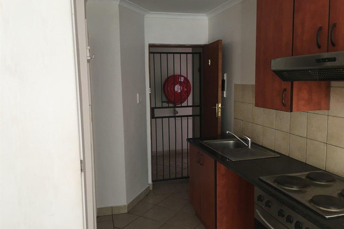 A functional kitchen featuring wood-finish cabinetry, dark countertops, a built-in electric hob with extractor, and direct access to a secure exterior area.