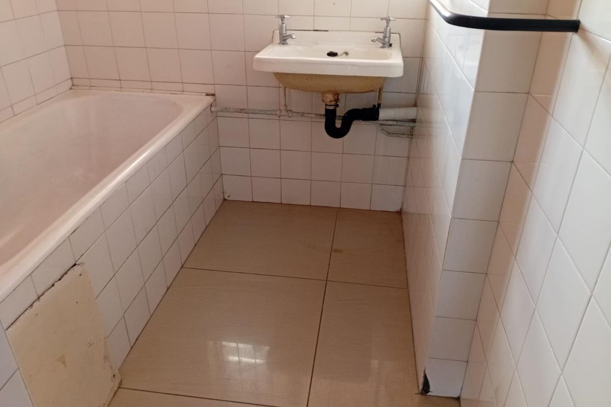 A dated bathroom featuring a standard bathtub, wall-mounted basin with exposed plumbing, and tiled walls and flooring.