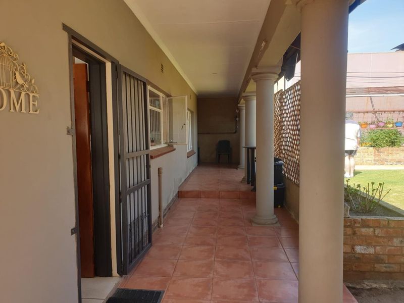 A covered patio area featuring tiled flooring, structural columns, and a security gate, providing access to the rear garden space.