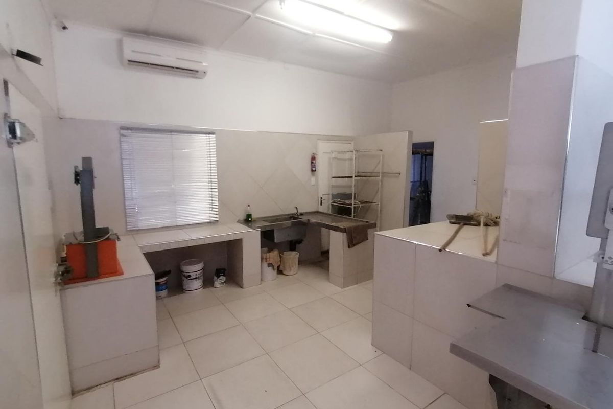 A functional commercial kitchen space featuring tiled surfaces, stainless steel sink, wall-mounted air conditioning unit, and industrial-style preparation areas.