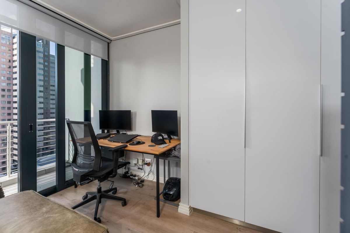 A modern bedroom featuring built-in wardrobes, laminate flooring, and large glass sliding doors providing access to a balcony with city views.