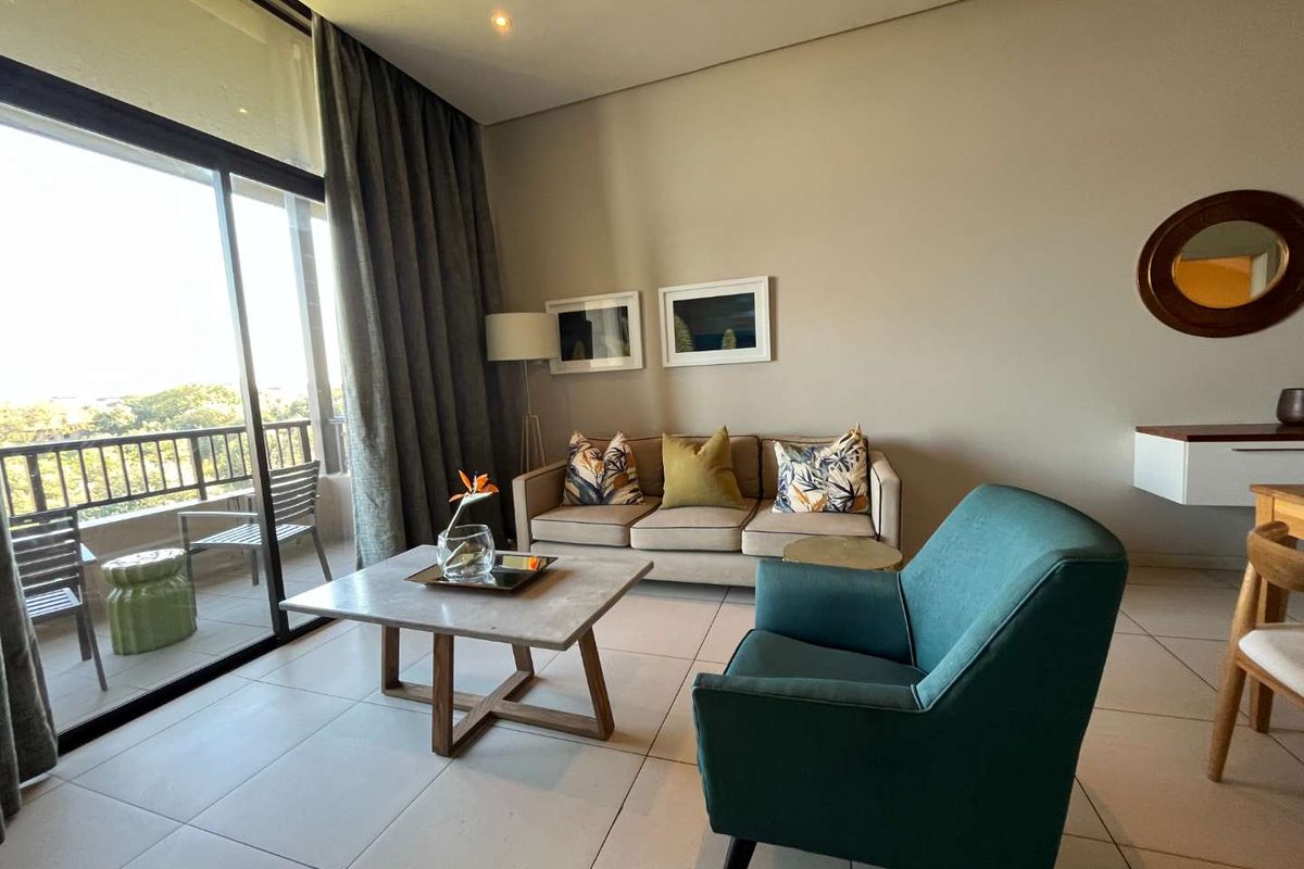 A bright living room featuring large sliding glass doors that open onto a private balcony, with neutral tiled flooring and modern finishes.