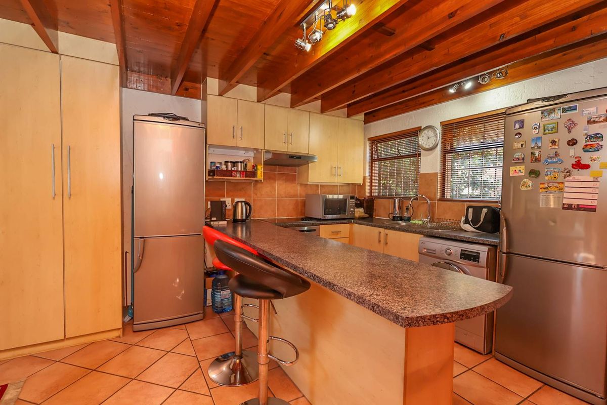 A functional kitchen featuring a breakfast bar, laminate cabinetry, granite countertops, and exposed timber ceiling beams, with tiled flooring throughout.