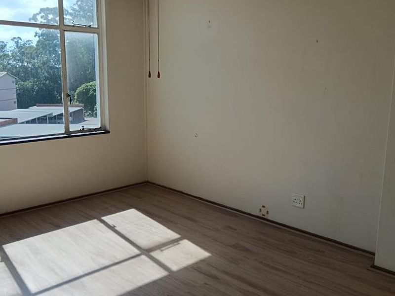 An empty bedroom featuring laminate flooring, a ceiling fan, and a large window providing natural light and an exterior view.