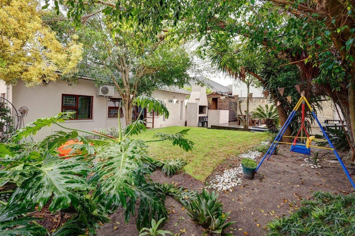 A private rear garden featuring a lawn, mature trees, and a built-in braai area, providing a functional outdoor space for relaxation and entertainment.