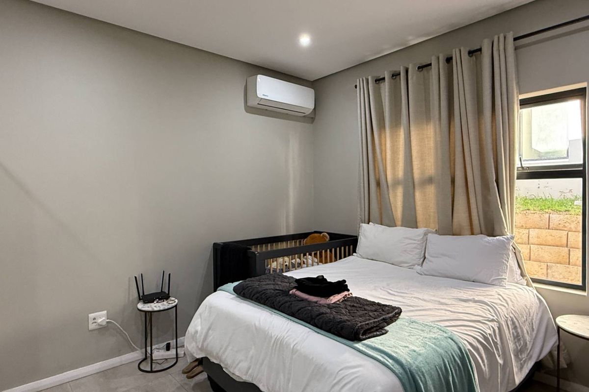 A well-maintained bedroom featuring neutral wall tones, tiled flooring, a wall-mounted air conditioning unit, and a window with curtain tracks.