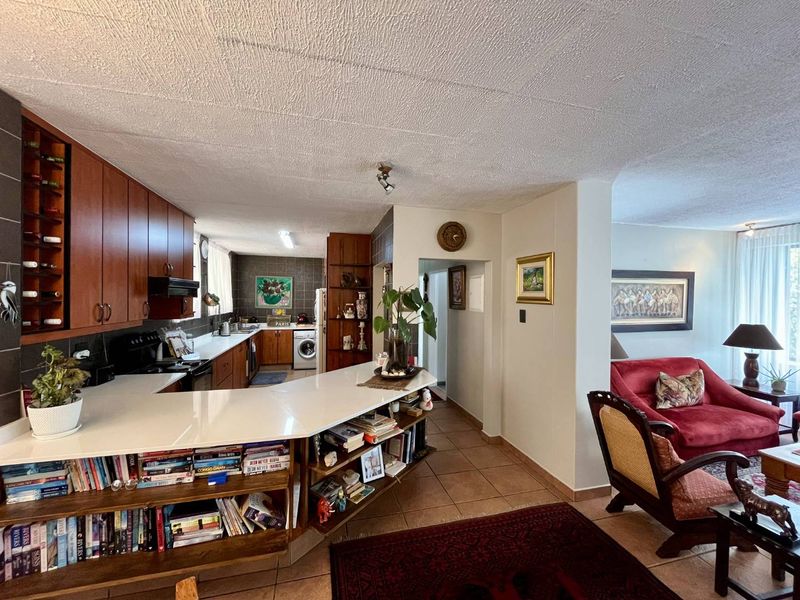 Open plan kitchen featuring wooden cabinetry, a breakfast bar, and integrated shelving, flowing into the adjacent living area.