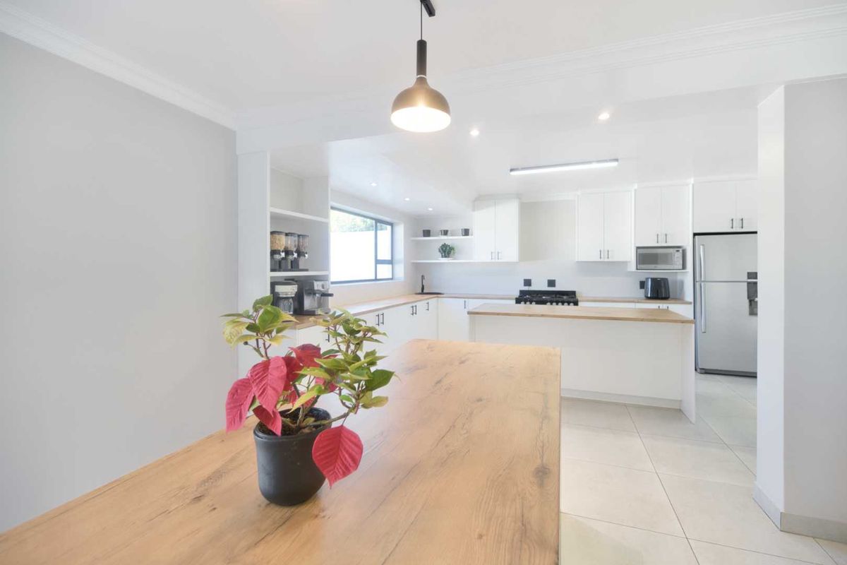 Modern kitchen featuring white cabinetry, wooden countertops, a central island, and integrated appliances, finished with clean tiled flooring and recessed lighting.