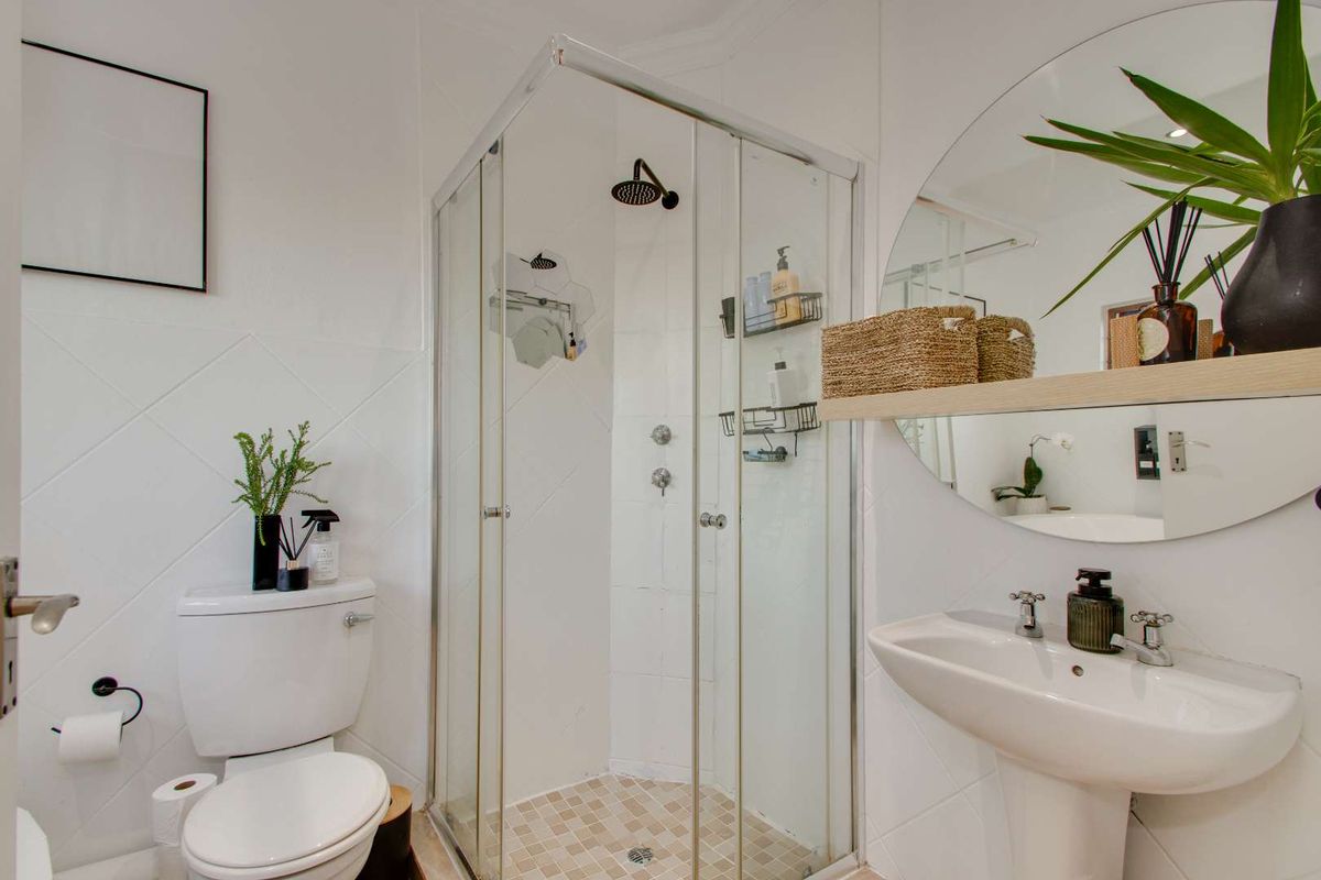 A compact, well-maintained bathroom featuring a corner shower enclosure, pedestal basin, and toilet with white tiled finishes.
