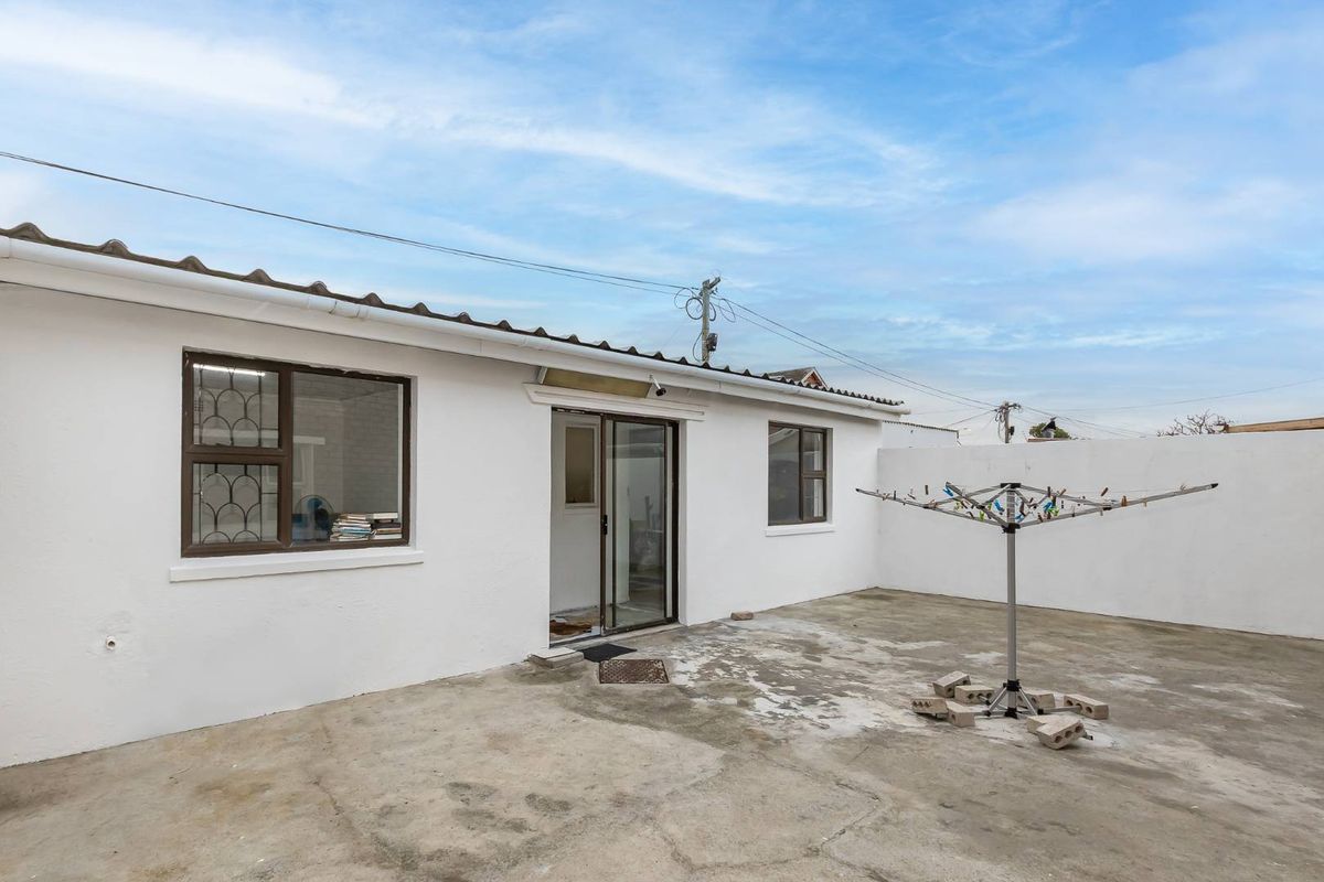 Rear exterior view featuring a concrete patio area, sliding glass door access, and secure window frames with security bars.