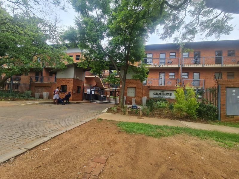 Front exterior view of The Circuits apartment complex, featuring a brick facade, gated entrance, and paved driveway access.