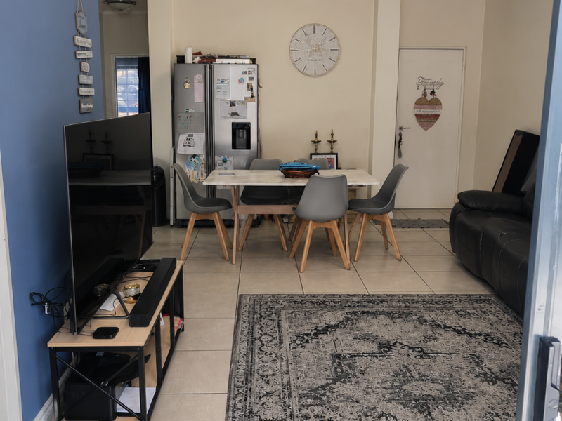 An open-plan living and dining area featuring neutral tiled flooring and a blue accent wall, providing a functional space for daily living.
