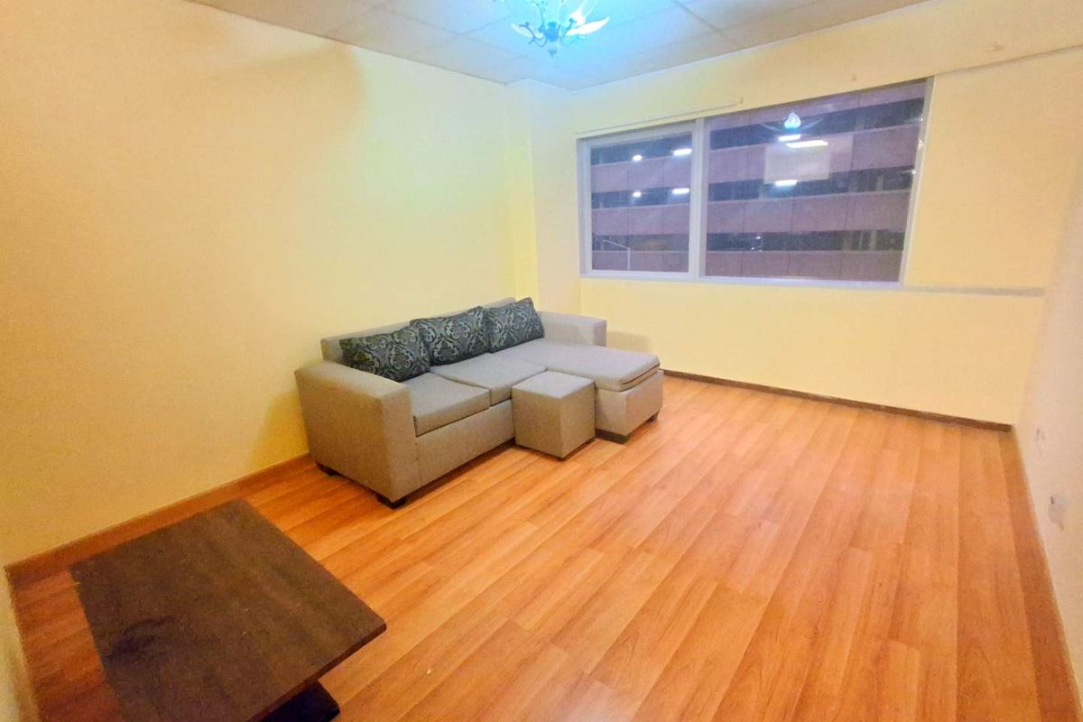 A living room featuring laminate wood-style flooring, a large window with city views, and a drop ceiling with a central light fixture.