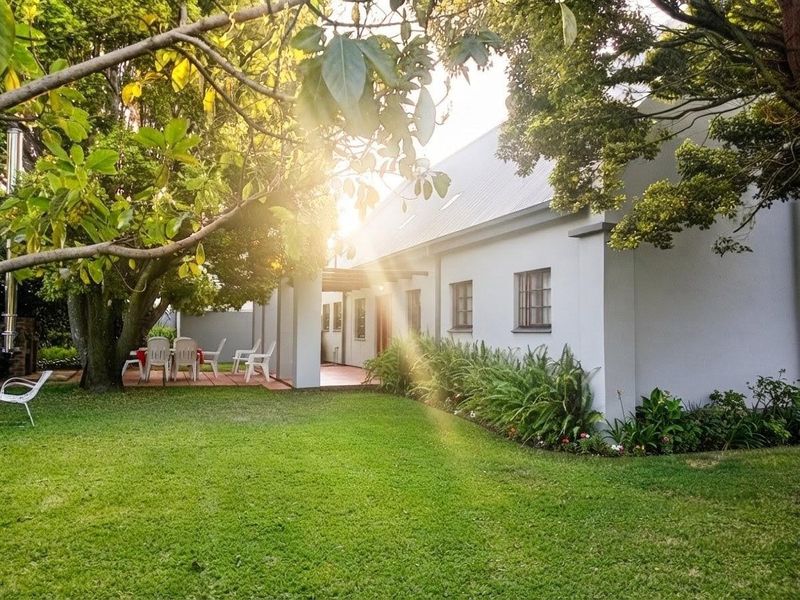 A view of the rear exterior of the house featuring a tiled patio area, well-maintained lawn, and mature garden landscaping.